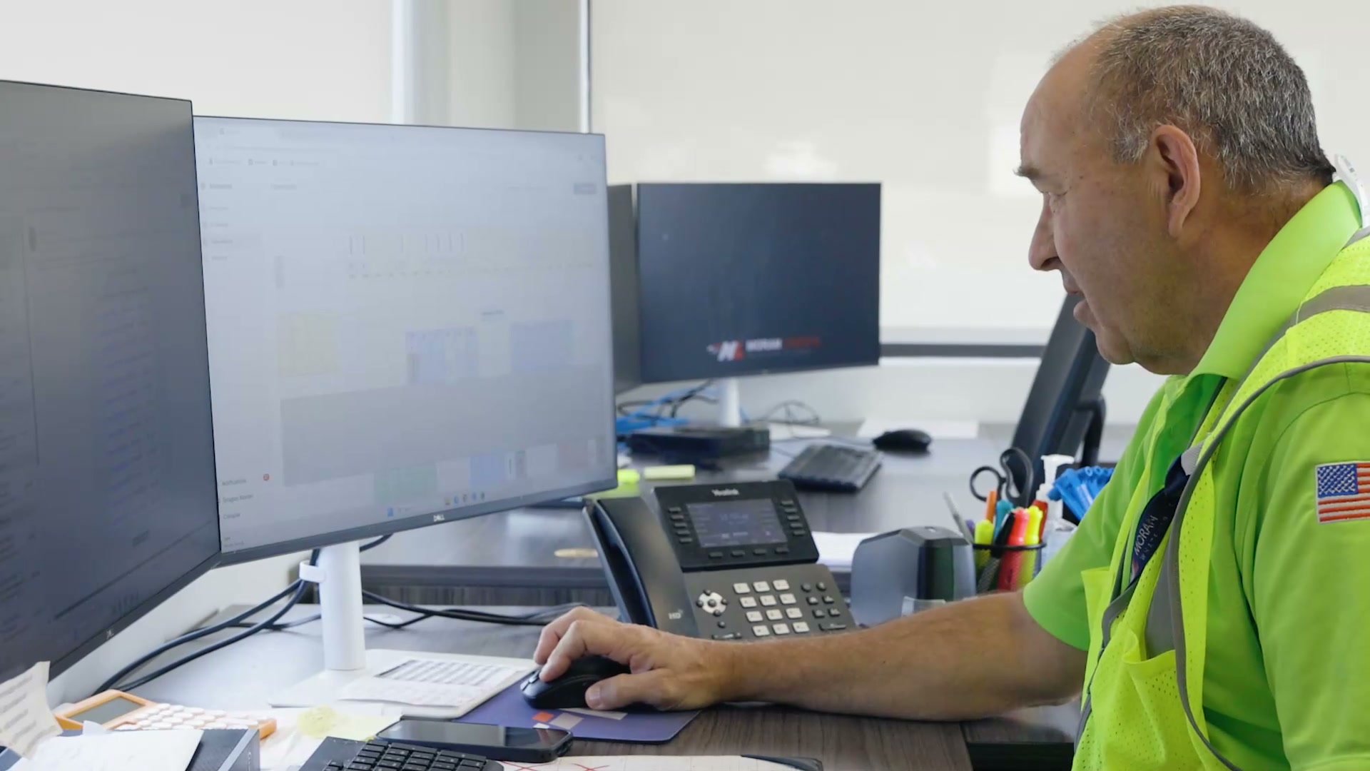 An operations coordinator at a Moran Logistics desk reading Movo on a widescreen monitor
