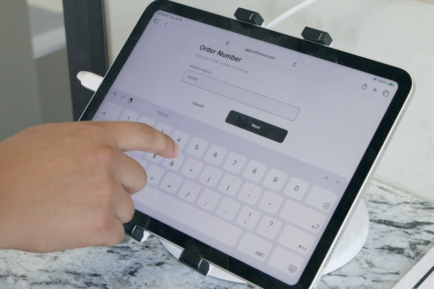 A driver typing an order number into the Movo check-in screen on an iPad at a gate counter